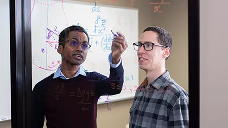 两个男学生在一面玻璃墙上做数学方程式.