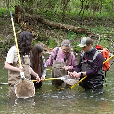 教授和学生们穿着水靴在齐腰深的河里进行科学实验.